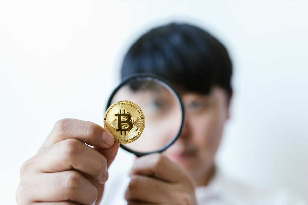 Close-up of a person examining a Bitcoin with a magnifying glass, highlighting cryptocurrency focus.